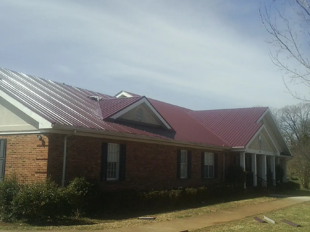 Red metal roof with gabled entries on a long brick building, from a Hail Damage Roof Repair job in Churchville