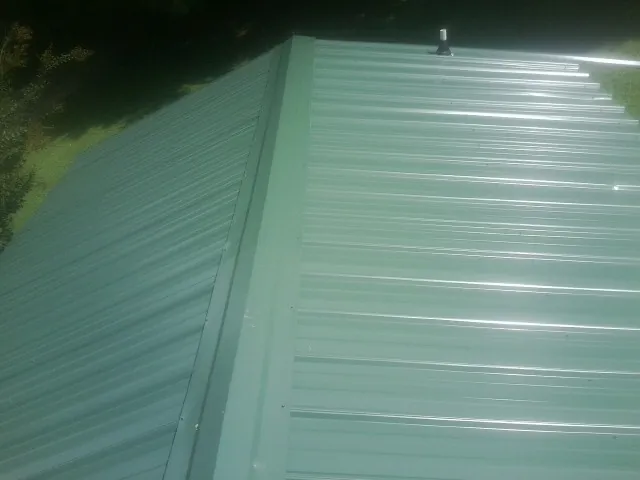 New green metal panels meeting at the ridge of a roof — Flat Roof Repair work by our crew in Churchville