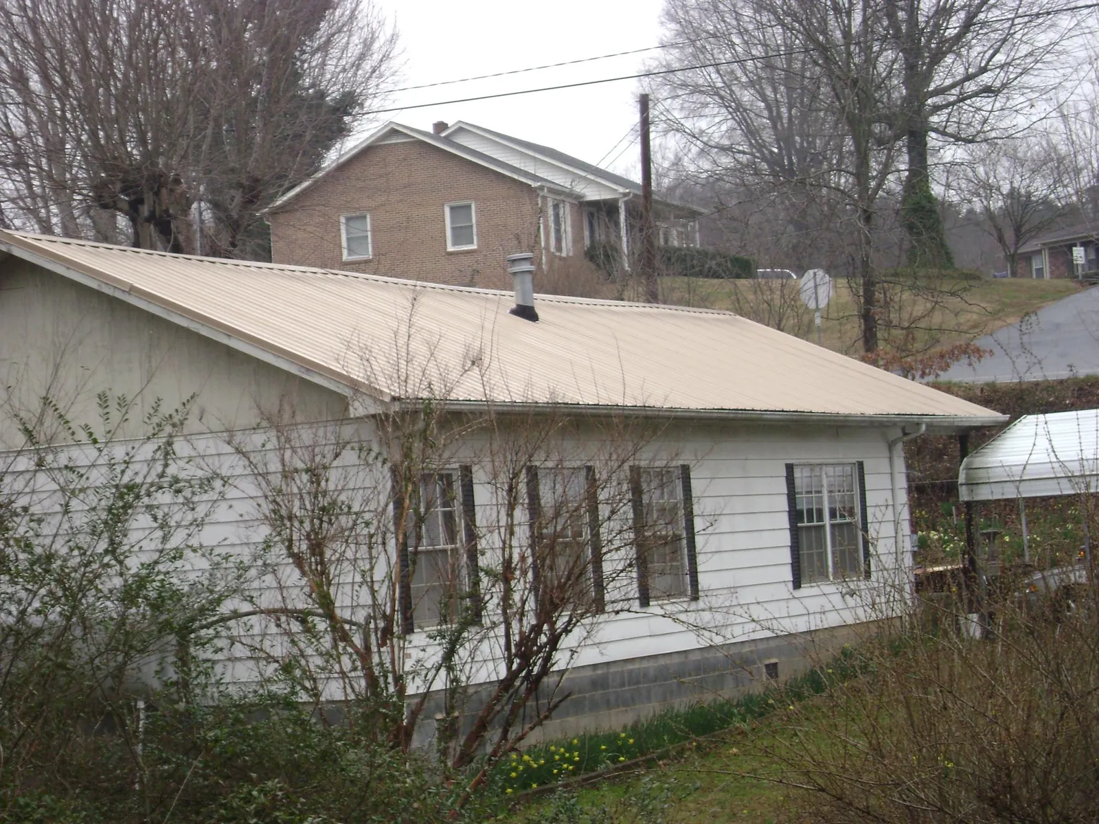 Tan metal roof on a white sided house set into a hillside — Commercial Roofing by Roofing Brothers in Churchville